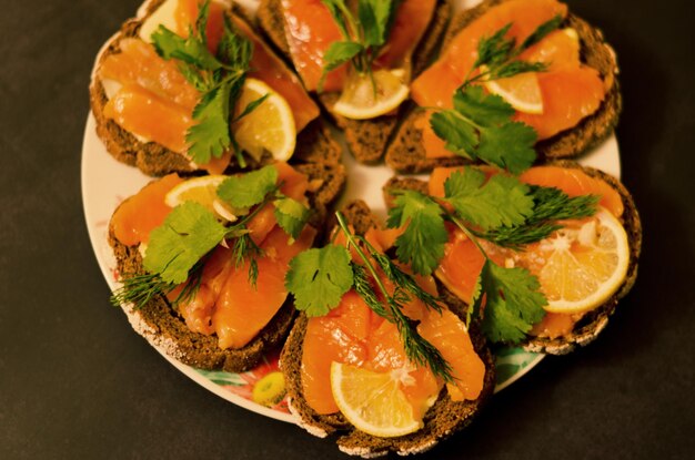 Sandwiches, Kanapee mit Räucherlachs, Butter, Kräuter auf dem Tisch. Ansicht von oben. Schwarzer Hintergrund