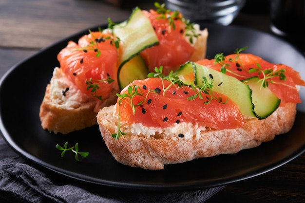 Sandwiches Lachstoast mit Frischkäse, Gurke, schwarzem Sesam und Microgreens auf altem Holztischhintergrund Meeresfrüchte Gesunde Lebensmittel Fotografie in zurückhaltender Ansicht von oben