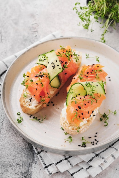 Sandwiches Lachstoast mit Frischkäse, Gurke, schwarzem Sesam und Microgreens auf grauem Betontischhintergrund Meeresfrüchte Gesunde Ernährung Draufsicht