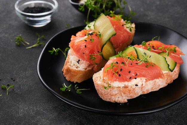 Sandwiches Lachstoast mit Frischkäse, Gurke, schwarzem Sesam und Microgreens auf schwarzem Hintergrund Meeresfrüchte Gesunde Ernährung Fotografie in zurückhaltender Ansicht von oben