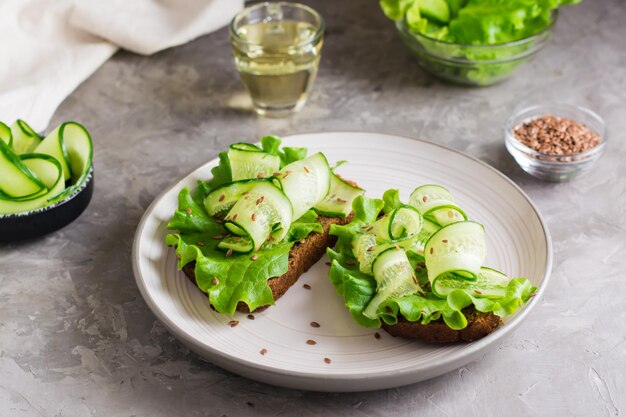 Sándwiches listos para comer con lechuga, pepino y semillas de lino en pan de centeno en un plato sobre la mesa Comida de dieta saludable