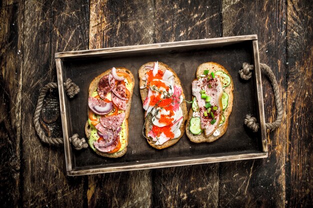 Sándwiches con mariscos, salami, tocino y verduras frescas en la mesa de madera.