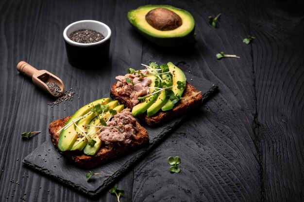 Sandwiches mit Avocado und Thunfisch microgreen Vollkornbrot Leckeres Frühstück oder Snack auf dunklem Hintergrund Draufsicht Langes Bannerformat