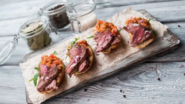 Sandwiches mit Fleisch. Mischung aus gekochtem Gemüse. Gehackte Zwiebel auf Bruschetta. Saftiges Kalbfleisch und frischer Rucola.