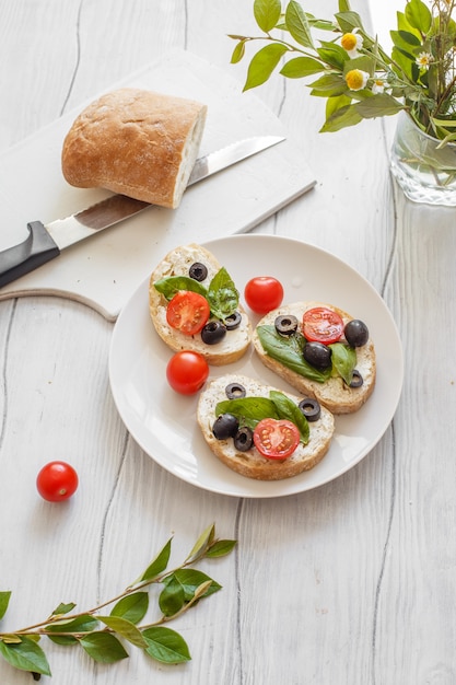 Sandwiches mit Frischkäsetomaten, Oliven und Basilikum auf einem weißen Holzbrett