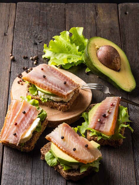 Sandwiches mit geräuchertem Fisch und Avocado auf einem Brett auf dunklem Hintergrund