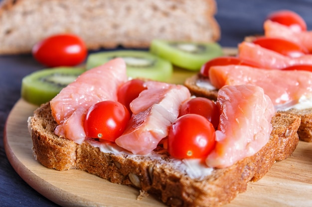 Sandwiches mit geräuchertem Lachs mit Butter- und Kirschtomaten auf schwarzem hölzernem Hintergrund