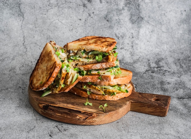 Sandwiches mit Kurkuma-Hähnchen-Gurken-Mikrogreens und hausgemachter Senf-Mayonnaise-Sauce auf einem Holzschneidebrett auf grauem Hintergrund