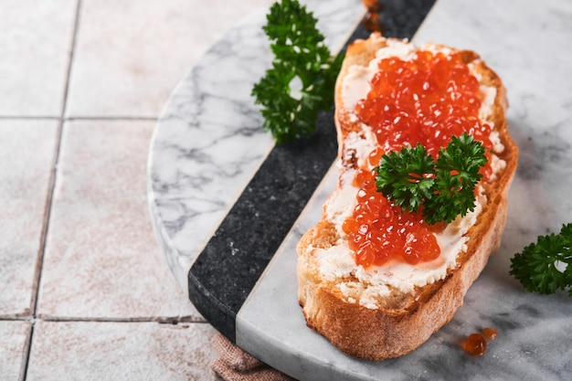 Sandwiches mit rotem Kaviar Lachsroter Kaviar in Schüssel und Sandwiches auf Marmorplatte auf altem grauem, rissigem Fliesentischhintergrund Draufsicht Kopierbereich