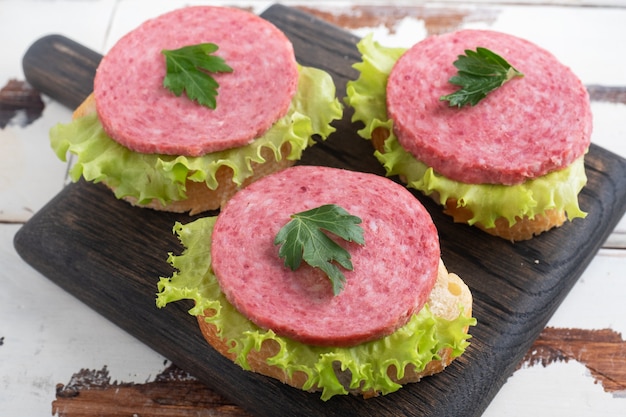 Sandwiches mit Salatblättern und geschnittener Salami-Wurst auf einem Holzbrett.