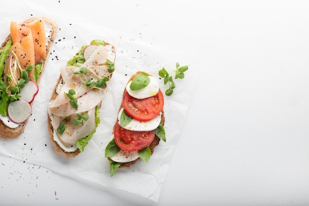 Sandwiches mit Schinken, Radieschen, Romano-Salat, Baby-Basilikum, Mascarpone-Käse, Caprese-Salat an einer weißen Wand. Speicherplatz kopieren. Draufsicht.