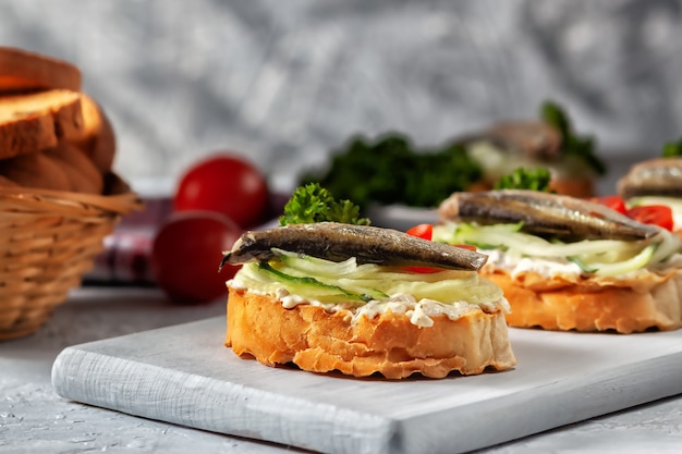 Sandwiches mit Sprotten auf gerösteten Brotscheiben. Geräuchertes Sprotten-Sandwich - Fisch, frische Gurke und Tomate.