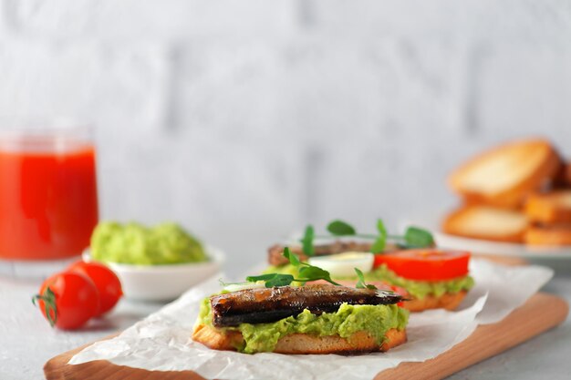 Sandwiches mit Sprotten auf gerösteten Brotscheiben. Sandwich mit geräuchertem Sprottenfisch, Avocado und Tomate