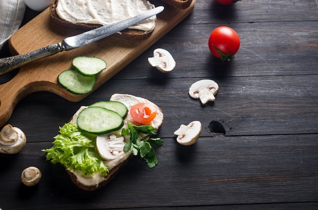 Sandwiches mit Weichkäse, Salat, Gurke, Tomaten und Pilzen auf einem dunklen Holztisch, Draufsicht. Gesundes Frühstück oder Mittagessen. Flach liegen.