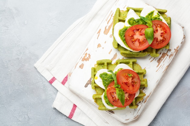 Sándwiches de oblea verde con espinacas y queso mozzarella, salsa pesto, tomates y albahaca sobre una vieja mesa de hormigón gris. Enfoque selectivo. Vista superior.