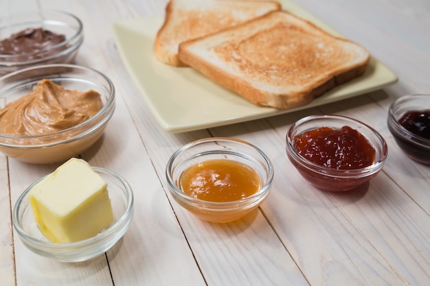 Sandwiches oder Toasts mit Erdnussbutter, Schokoladenpaste und Erdbeere, Johannisbeere und Aprikosengelee oder Marmelade auf weißem Holztisch