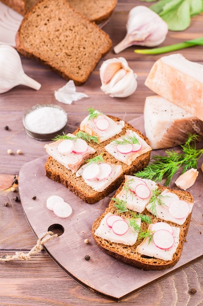 Sandwiches de pan de centeno, tocino salado, rábano y eneldo sobre una tabla para cortar sobre una mesa de madera