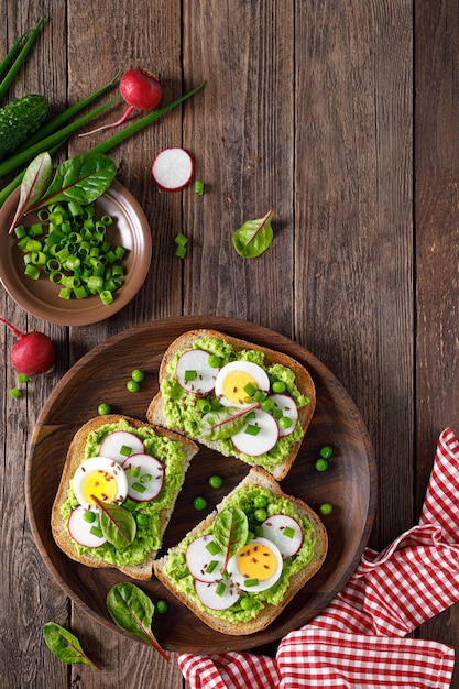 Sándwiches con pan integral hummus o puré de guisantes frescos rábano pepino huevo cocido cebolla verde y acelga