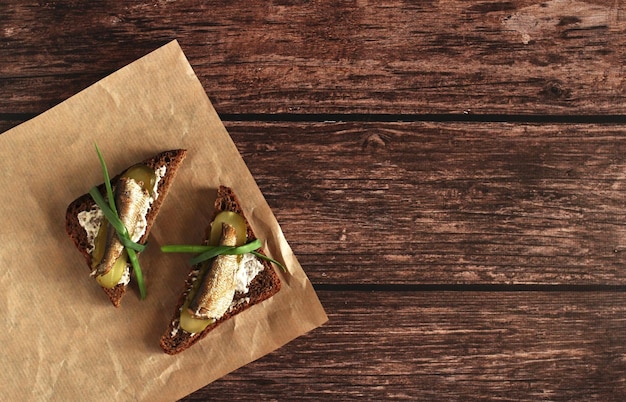 Sándwiches de pan integral con pepinillos, cebollas, ajo y espadines sobre un fondo de madera