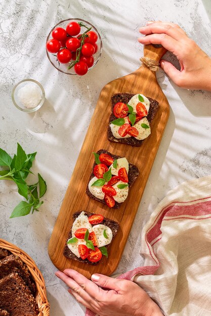 Sándwiches de pan integral con queso, tomates y hojas de albahaca, vista superior. Concepto de merienda saludable.