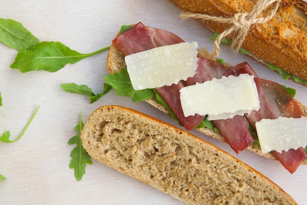 Sándwiches con pan integral, rúcula, queso parmesano y bresaola. Espacio libre para un texto.