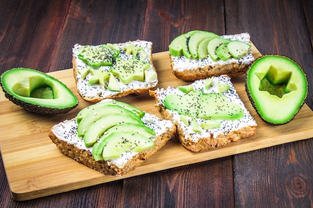 Sándwiches de pan con rodajas, estrellas, corazones de aguacate y requesón sobre fondo de madera.