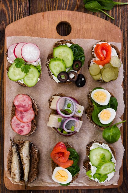 Sándwiches pequeños con verduras, pescado y salchichas a bordo sobre fondo de madera Vista superior