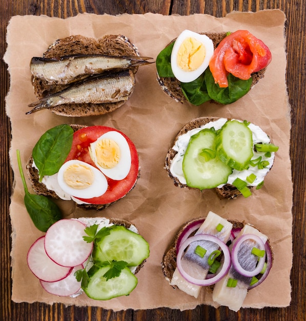 Sándwiches pequeños con verduras pescado y salchichas sobre fondo de madera