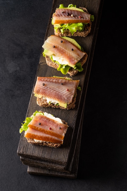 Sándwiches de pescado ahumado y aguacate en una placa sobre un fondo oscuro