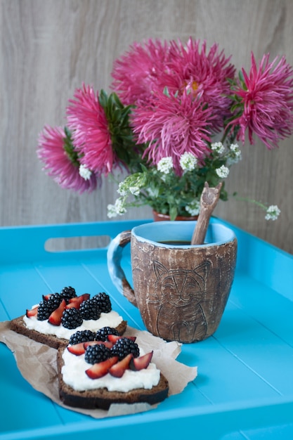 Sandwiches con queso dulce y bayas, una taza de café en la mesa de madera azul