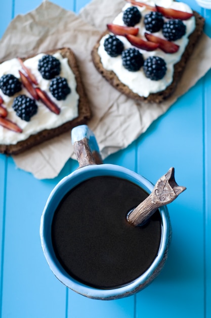 Sandwiches con queso dulce y bayas, una taza de café en la superficie de madera azul