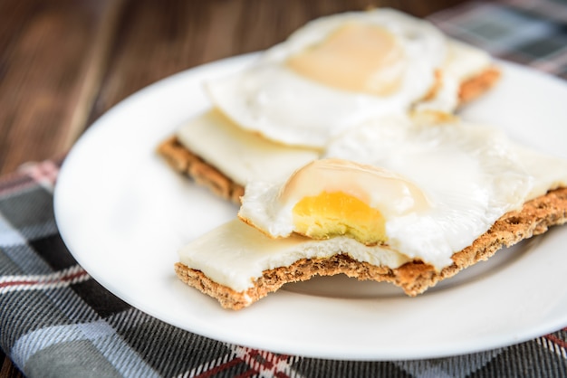 Sándwiches con queso suave y huevo sobre pan de centeno crujiente en madera oscura.