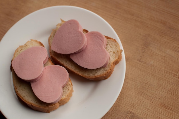 Sándwiches de salchicha en forma de corazones en una placa blanca sobre un fondo de madera