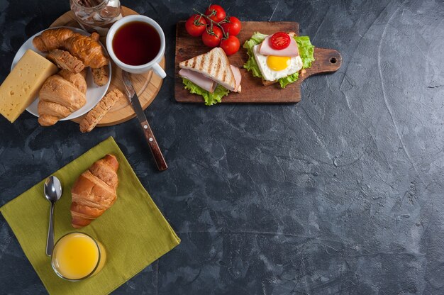 Sándwiches de salchichas y huevo frito. Desayuno con zumo de naranja y croissant sobre tablas rústicas de madera.