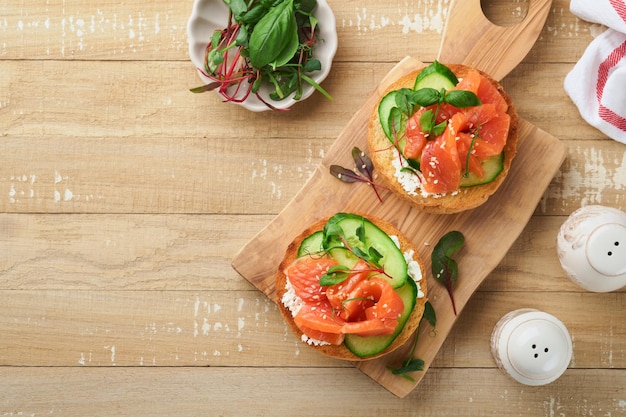 Sandwiches de salmón ahumado abiertos con queso crema pepino semillas de sésamo microgreens espinacas y hojas de guisantes en un fondo de madera vieja ligera comida saludable para el desayuno bocadillo delicioso vista superior