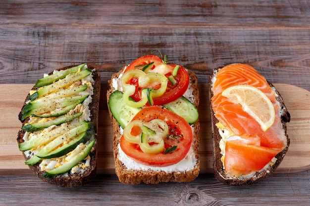 Sándwiches con salmón, tomates, pepinos, huevo y queso en una tabla de madera