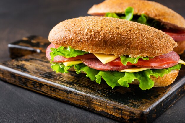 Sándwiches saludables con pan de salvado, queso, lechuga, tomate y salami en rodajas sobre un soporte de madera rústica. Concepto de desayuno. Vista superior.