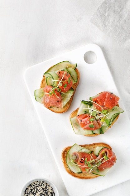 Sándwiches saludables tostadas con pepinos en rodajas de salmón y microvegetales Aperitivos de bruschetta en pizarra blanca y fondo blanco