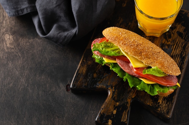 Sándwiches saludables con verduras y salami en rodajas en un soporte de madera rústico cerca de jugo de naranja