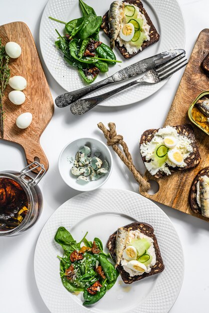 Sandwiches con sardinas, huevos, pepino y queso crema en mesa blanca