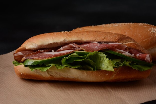 Sándwiches submarinos frescos con tocino, queso, tomate, lechuga, pepinos y cebollas sobre fondo oscuro