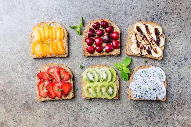 sándwiches de tostadas con mantequilla de maní, bayas y frutas melocotón, fresa, plátano, cereza, kiwi y fruta del dragón