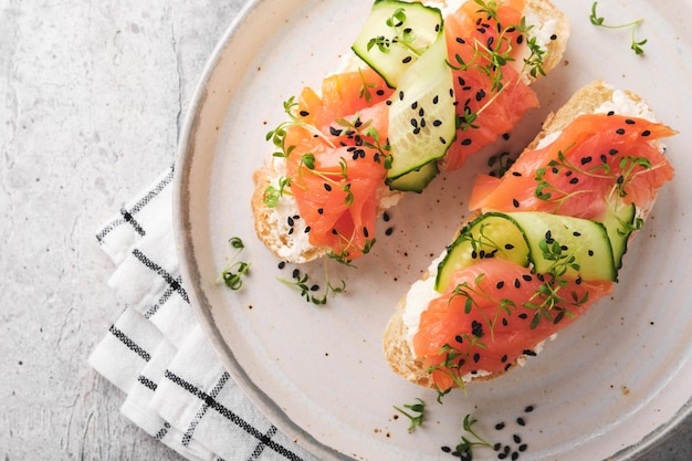 Sándwiches Tostadas de salmón con queso crema pepino sésamo negro y microgreens sobre fondo de mesa de hormigón gris Mariscos Comida saludable Vista superior