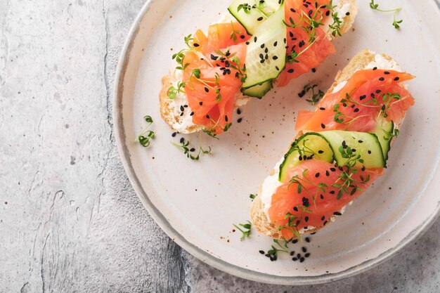 Sándwiches Tostadas de salmón con queso crema pepino sésamo negro y microgreens sobre fondo de mesa de hormigón gris Mariscos Comida saludable Vista superior