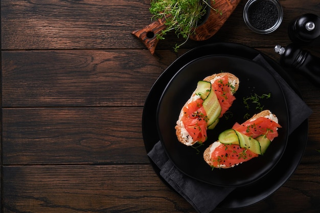 Sándwiches Tostadas de salmón con queso crema pepino sésamo negro y microvegetales sobre fondo de mesa de madera vieja Mariscos Comida saludable Fotografía en clave baja Vista superior