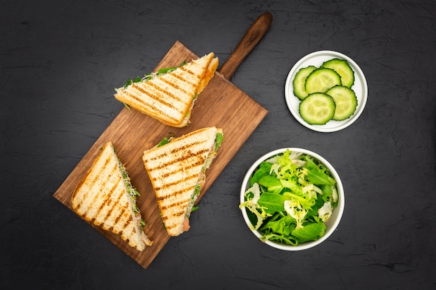 Sandwiches triangulares en tabla de cortar con rodajas de ensalada y pepino