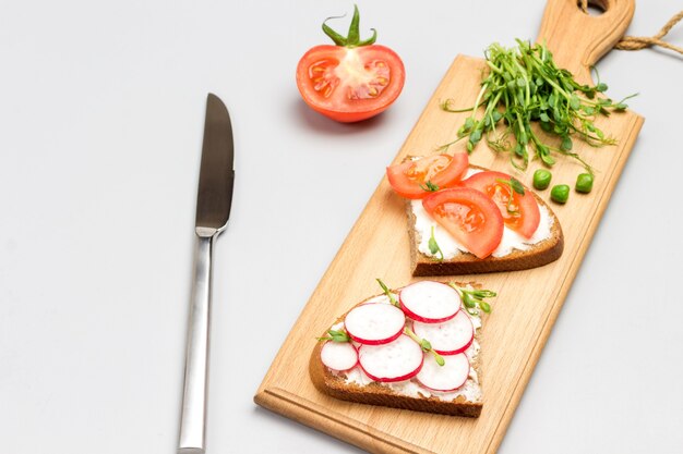 Sándwiches vegetarianos con tomates y rábanos en tabla de cortar