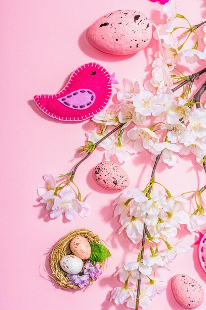 Foto sanfte osterkomposition mit kirschblüten und handgefertigten filzvögeln, dekorative eier und nest, niedliche kaninchen, harter, heller, dunkler schatten, rosa hintergrund, draufsicht