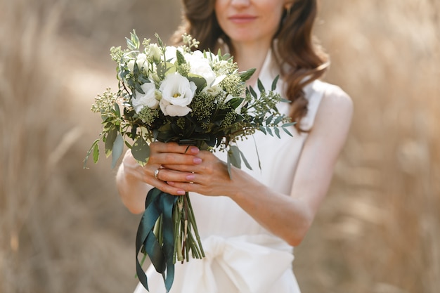 Sanfter Brautstrauß mit Spitze und Bändern. stilvoller Hochzeitsstrauß in den Händen der Braut. lächelnde Frau mit Strauß der weißen Blumen schließen. schöne und stilvolle Blumenkomposition im Freien.