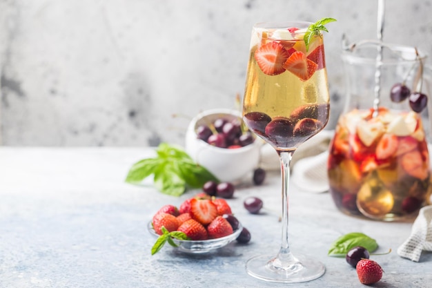 Sangria de vinho branco ou ponche com frutas vermelhas e gelo em copo e pincher. Sangria de fruta refrescante caseira.